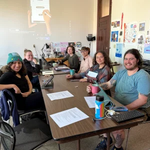 A group of artists sitting in a classroom with iPads smiling at camera.